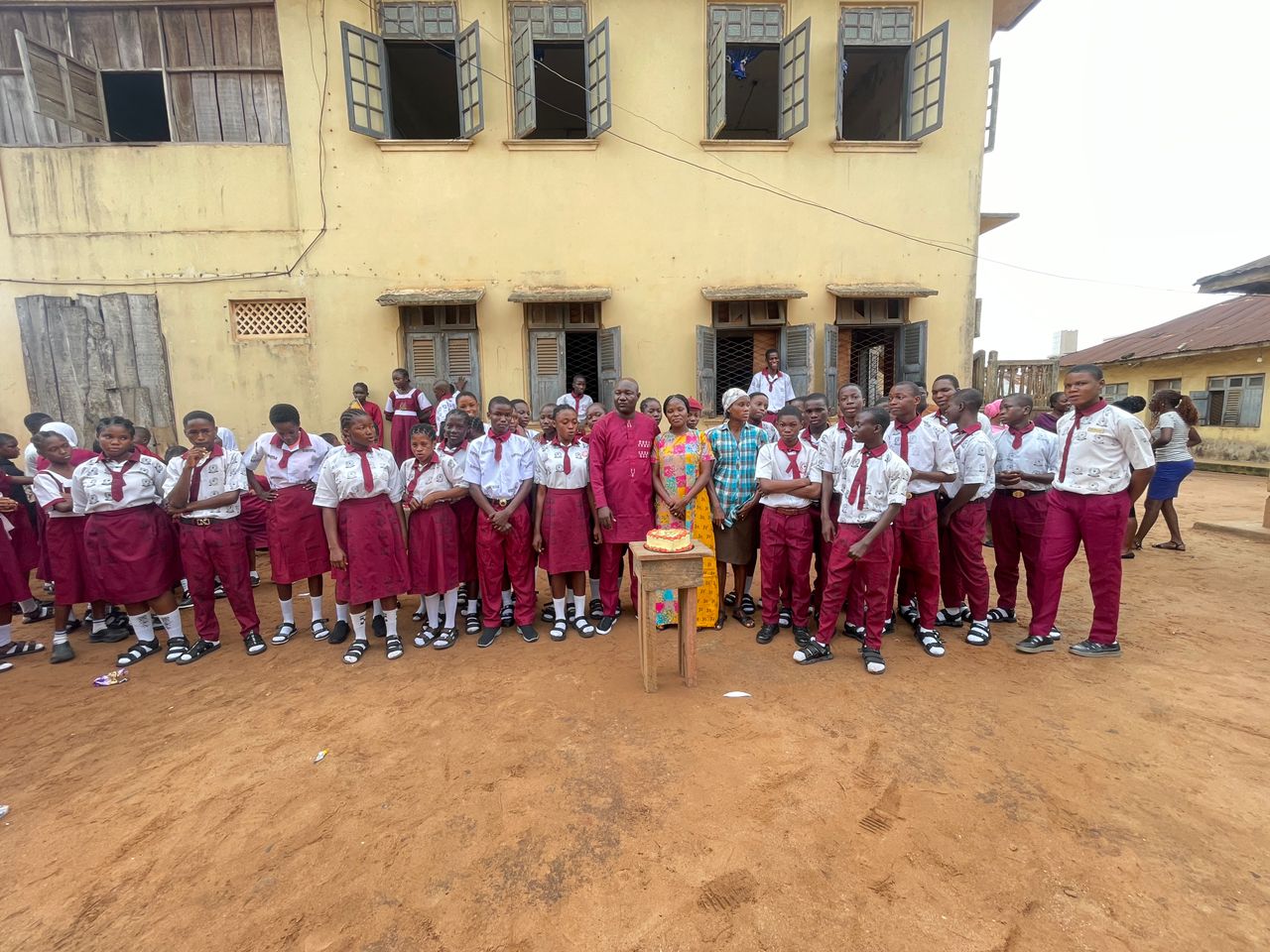 Students and school proprietors gathered outdoors for a celebration with cake
